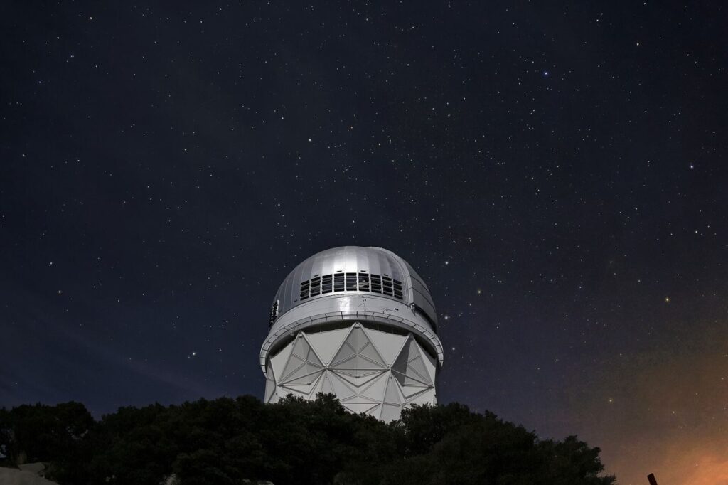 telescope silhouetted under a star-filled night sky