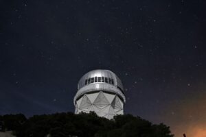 telescope silhouetted under a star-filled night sky