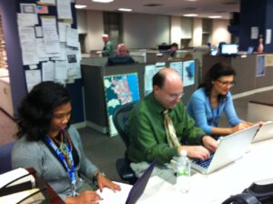 A journalist at work in a newsroom surrounded by screens and notes